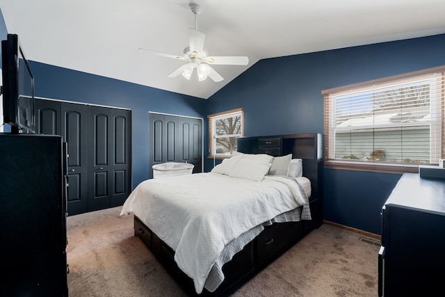 carpeted bedroom with two closets, visible vents, ceiling fan, vaulted ceiling, and baseboards