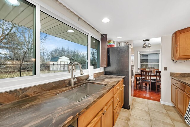 kitchen with brown cabinets, freestanding refrigerator, light tile patterned flooring, a sink, and recessed lighting