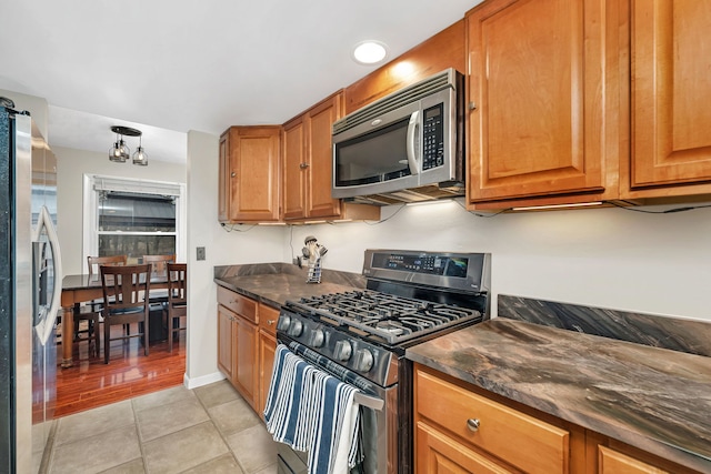 kitchen with dark countertops, light tile patterned floors, appliances with stainless steel finishes, and brown cabinets