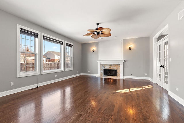 unfurnished living room with dark wood-style flooring, french doors, visible vents, a stone fireplace, and baseboards