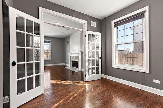 unfurnished living room with baseboards, visible vents, dark wood finished floors, french doors, and a high end fireplace