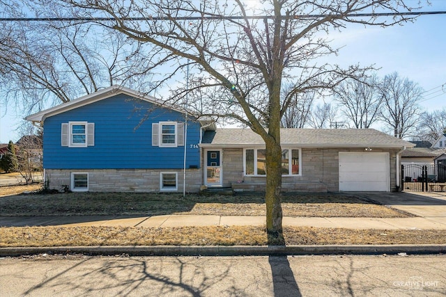 split level home featuring concrete driveway, an attached garage, and stone siding