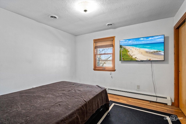 unfurnished bedroom with visible vents, baseboard heating, wood finished floors, and a textured ceiling