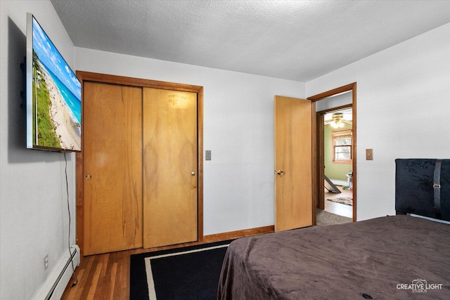 bedroom featuring a baseboard radiator, a textured ceiling, a closet, and wood finished floors