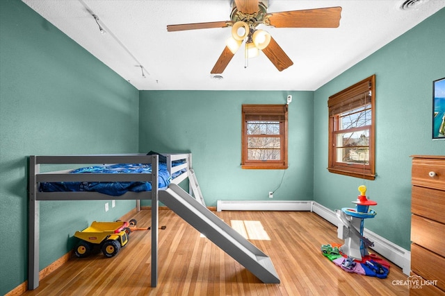 bedroom with visible vents, ceiling fan, baseboards, baseboard heating, and wood finished floors