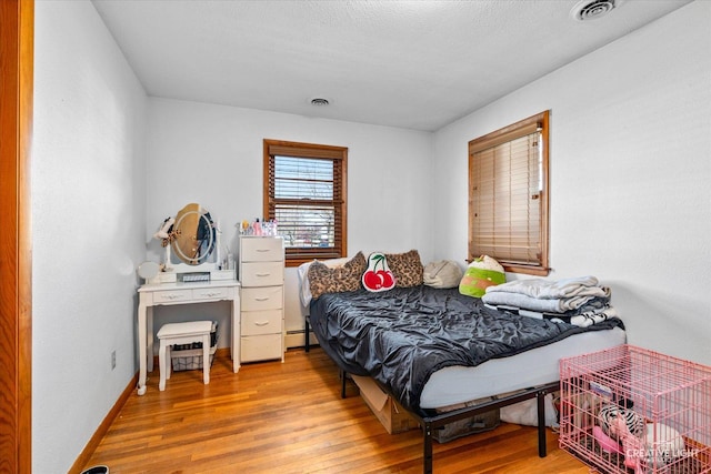 bedroom featuring a baseboard heating unit, wood finished floors, visible vents, and baseboards