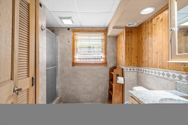 bathroom with vanity, visible vents, a drop ceiling, a shower stall, and tile walls