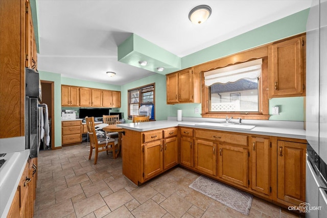 kitchen featuring a peninsula, light countertops, brown cabinets, and a sink