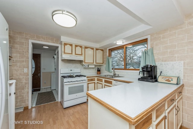 kitchen featuring tile walls, gas range gas stove, light countertops, a sink, and under cabinet range hood