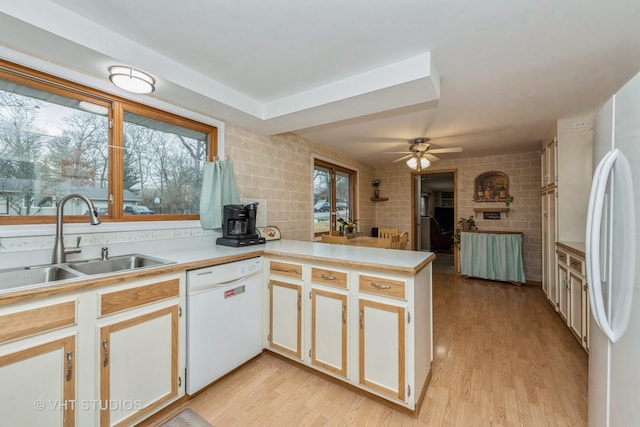 kitchen with light wood-style flooring, a peninsula, white appliances, a sink, and light countertops