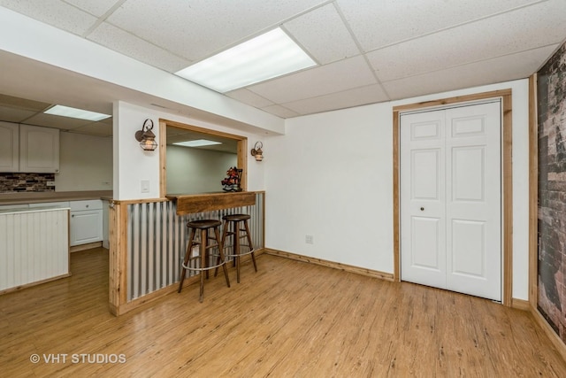 kitchen with light wood-style floors, a kitchen bar, baseboards, and a drop ceiling