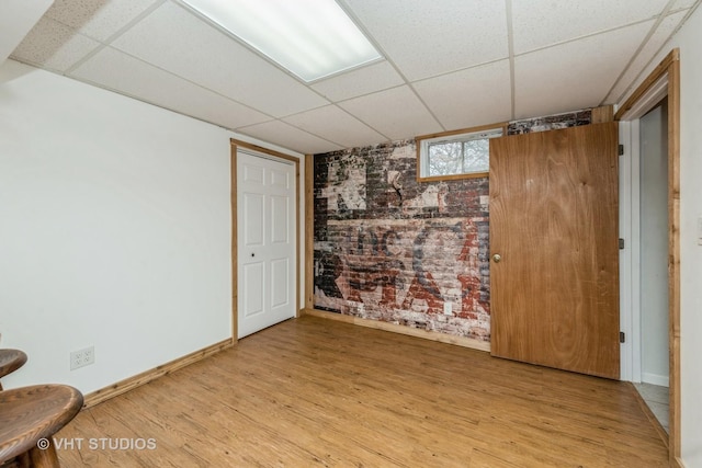 below grade area featuring light wood-style flooring, baseboards, and a drop ceiling