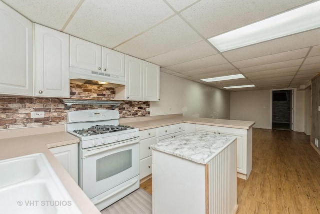 kitchen featuring under cabinet range hood, a peninsula, white cabinets, light countertops, and white gas range oven