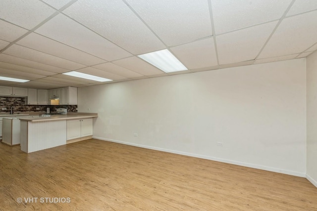 kitchen with a drop ceiling, a peninsula, light countertops, light wood-type flooring, and tasteful backsplash