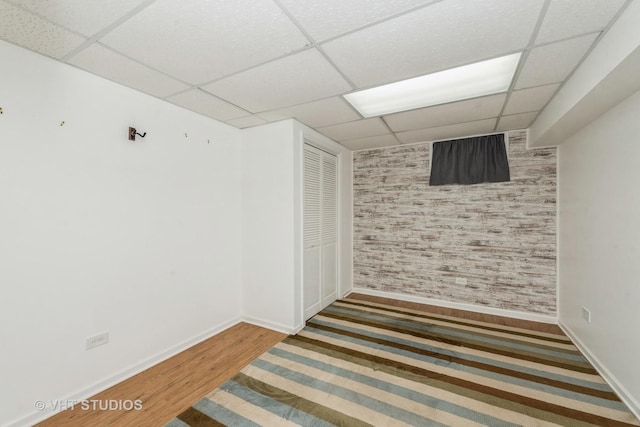 unfurnished room with an accent wall, wood finished floors, a paneled ceiling, and baseboards