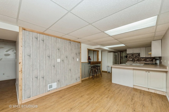 kitchen featuring light wood-style floors, a paneled ceiling, visible vents, and decorative backsplash