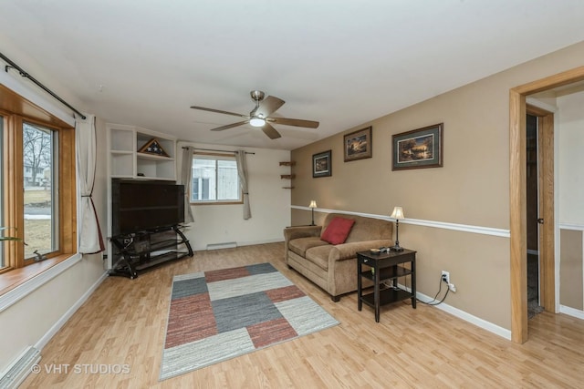 living area with a ceiling fan, a baseboard radiator, baseboards, and wood finished floors