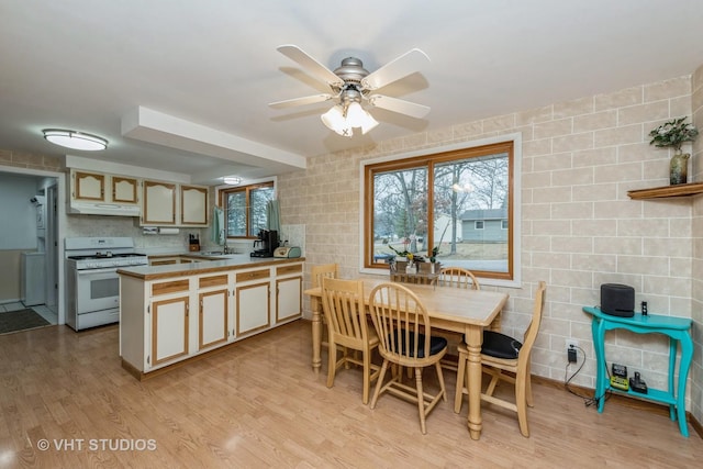 kitchen with light wood-style flooring, a sink, a peninsula, under cabinet range hood, and white gas range oven