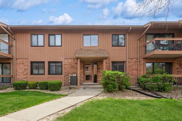 multi unit property featuring central AC unit, a balcony, brick siding, and a front lawn