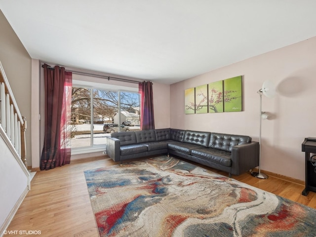 living room featuring light wood-style floors, baseboards, and stairs