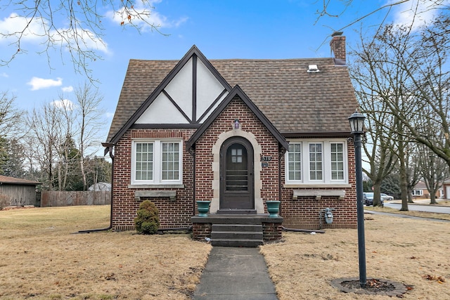 tudor house with brick siding, roof with shingles, a chimney, and stucco siding