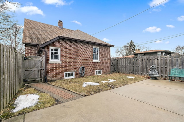 view of side of property featuring roof with shingles, brick siding, a chimney, and a fenced backyard