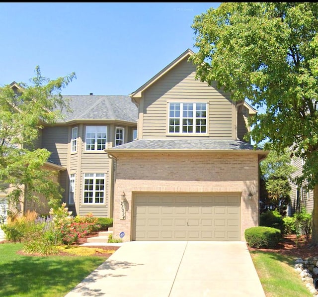 traditional-style house featuring a garage, concrete driveway, brick siding, and roof with shingles