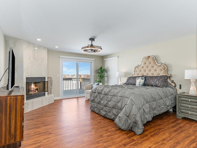 bedroom featuring a premium fireplace, recessed lighting, wood finished floors, and access to exterior