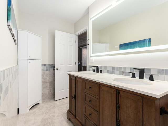 full bath with double vanity, wainscoting, a sink, and tile walls