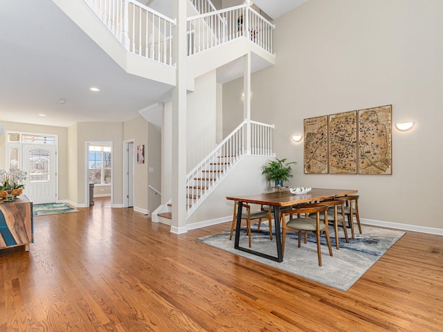 dining area with baseboards, a towering ceiling, stairway, wood finished floors, and recessed lighting