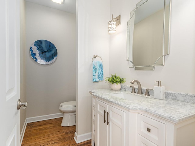 bathroom with toilet, baseboards, wood finished floors, and vanity