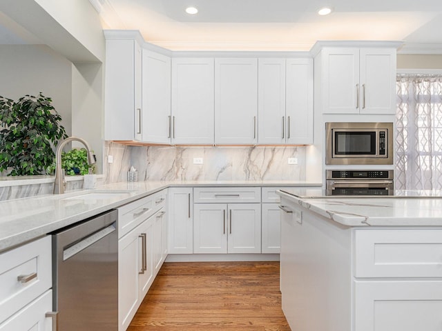 kitchen with light wood-style flooring, decorative backsplash, appliances with stainless steel finishes, white cabinetry, and a sink