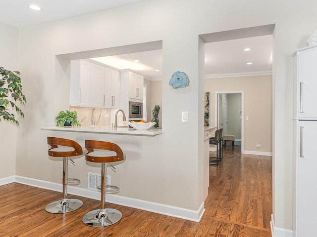 kitchen featuring stainless steel microwave, wood finished floors, light countertops, a kitchen bar, and white cabinetry