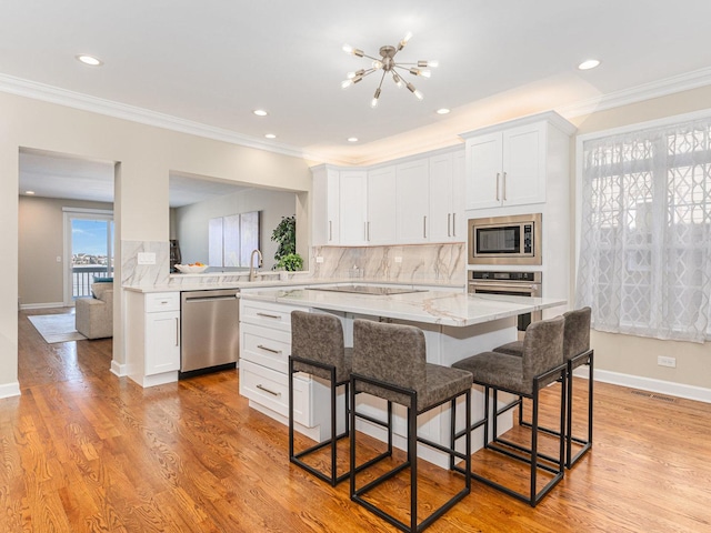 kitchen with light wood finished floors, stainless steel appliances, backsplash, white cabinetry, and a kitchen breakfast bar