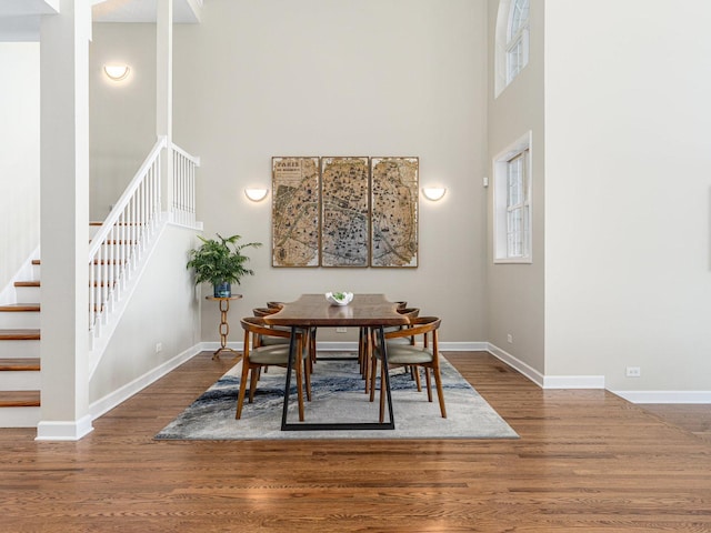 dining space with stairway, a high ceiling, baseboards, and wood finished floors