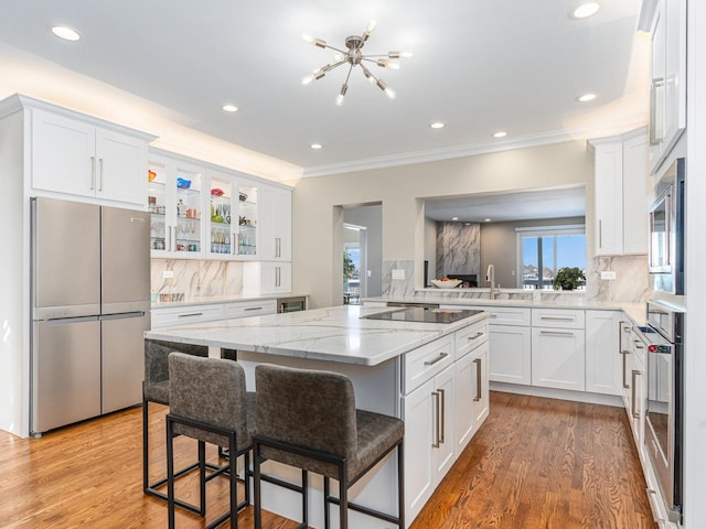 kitchen featuring light stone counters, stainless steel appliances, white cabinets, light wood-type flooring, and a kitchen bar