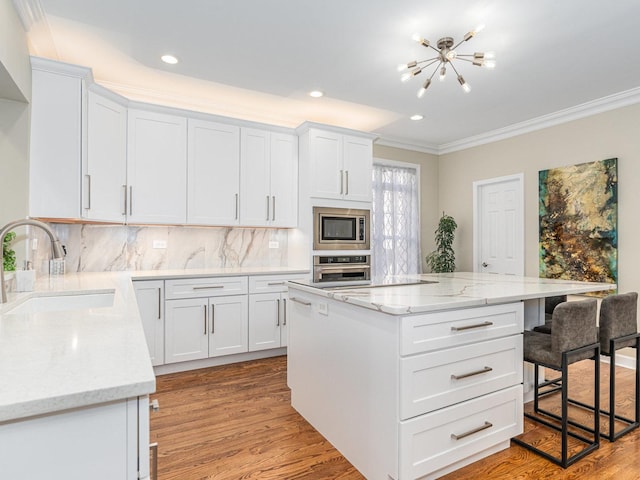 kitchen with a sink, appliances with stainless steel finishes, light wood-type flooring, a kitchen bar, and crown molding