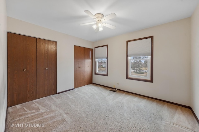 unfurnished bedroom featuring light carpet, ceiling fan, baseboards, and multiple closets