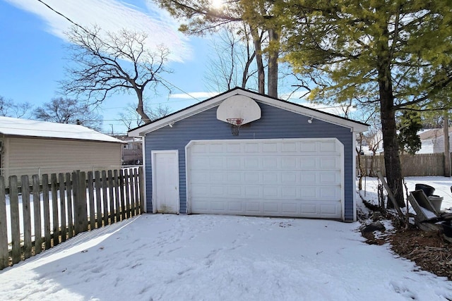 snow covered garage with a garage and fence