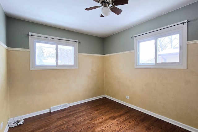 spare room with dark wood-style floors, a wealth of natural light, visible vents, and baseboards