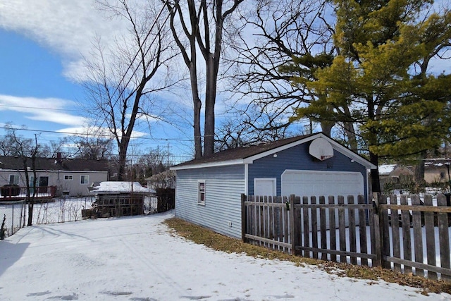 snow covered garage featuring a garage and fence