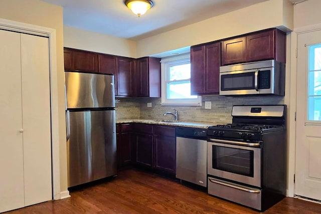 kitchen with stainless steel appliances, a sink, backsplash, light stone countertops, and dark wood finished floors