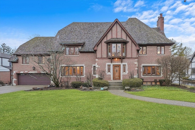 tudor-style house with brick siding, a chimney, a front yard, a garage, and driveway