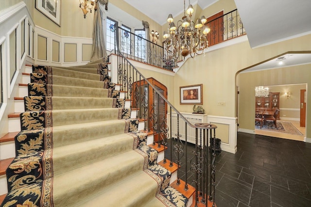 stairway with arched walkways, crown molding, a decorative wall, and an inviting chandelier