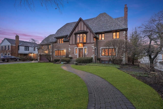 view of front facade featuring a garage, brick siding, driveway, a lawn, and a chimney