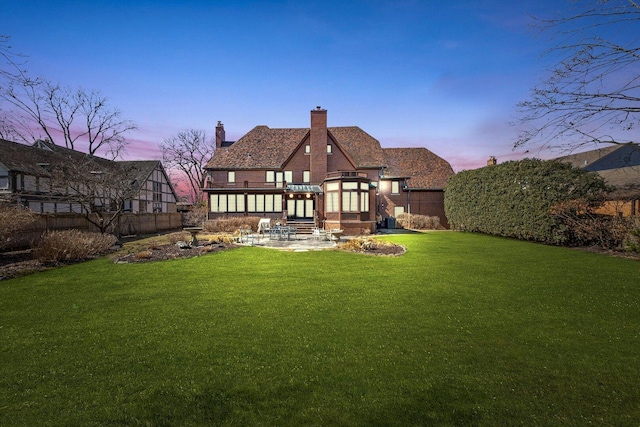 back of house at dusk with a chimney, fence, and a yard