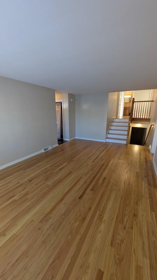 unfurnished living room featuring stairway, visible vents, light wood-style flooring, and baseboards