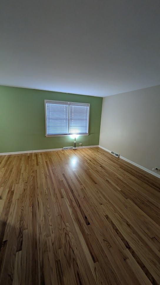 spare room with baseboards, visible vents, and wood finished floors