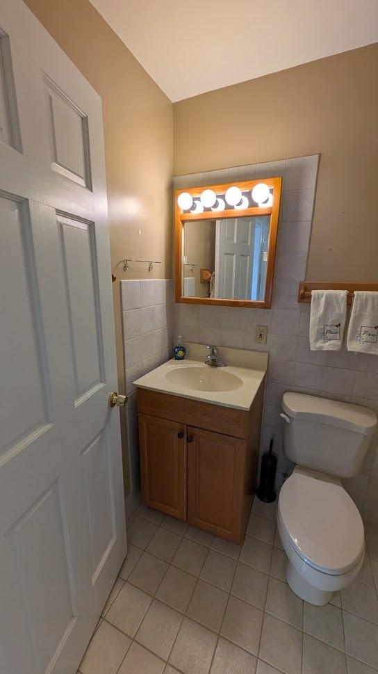 bathroom with tile patterned floors, tile walls, toilet, and vanity