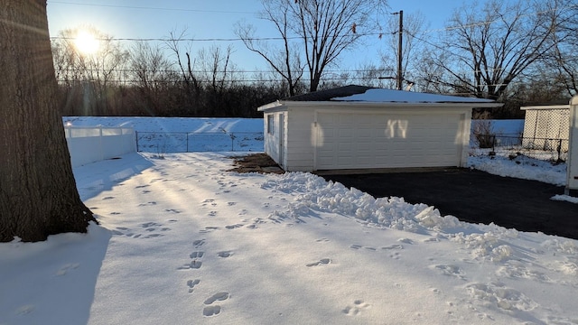 view of snowy exterior featuring a garage, an outdoor structure, and fence